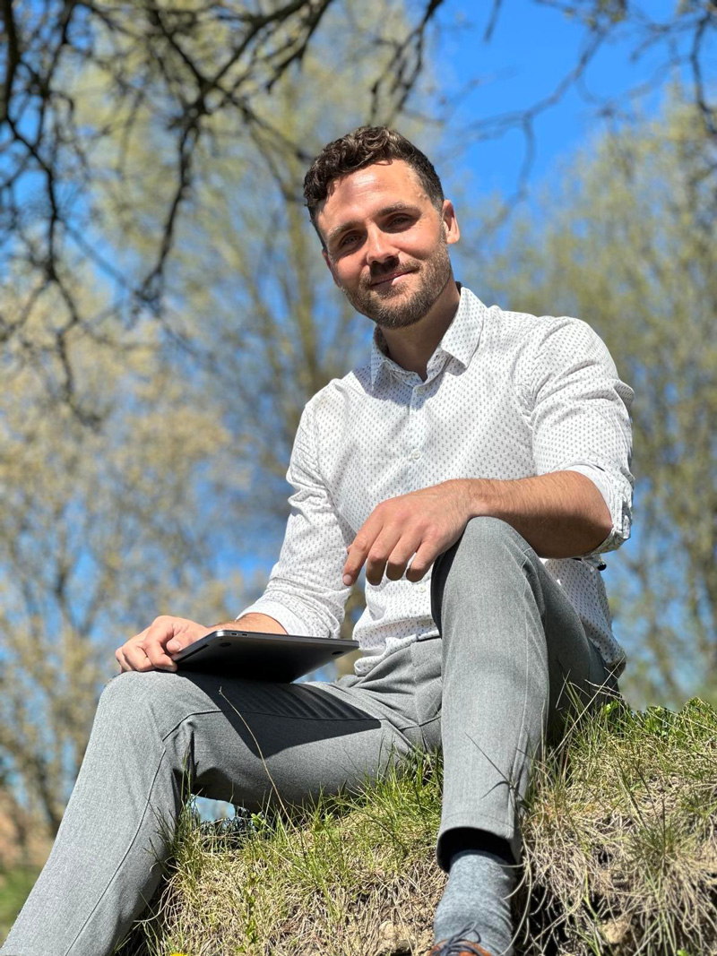 Træneren sidder udendørs og holder sin bærbare computer.